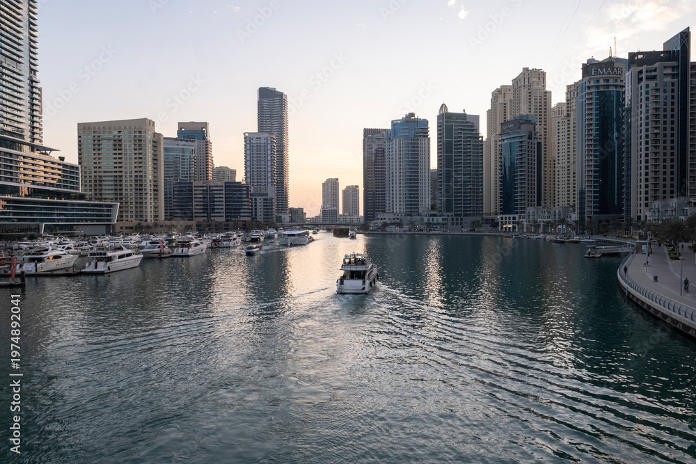 Obraz premium 12.12.2025 Dubai, UAE. Luxury yachts and boats moored in Dubai Marina at sunset. Stunning view of skyscrapers and modern architecture in UAE with golden sky reflection in the water. High-end lifestyle