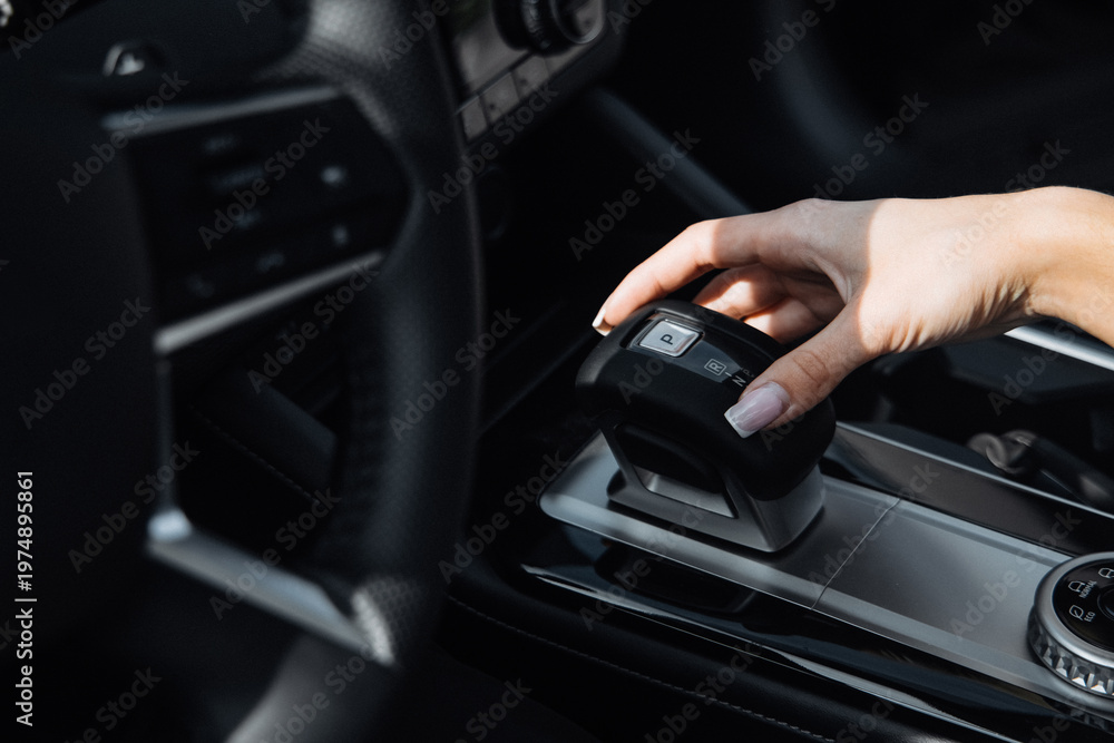 Fototapeta premium Driver's hand operating gear shift in modern car interior, showcasing sleek dashboard design and high-quality materials in a contemporary vehicle setting