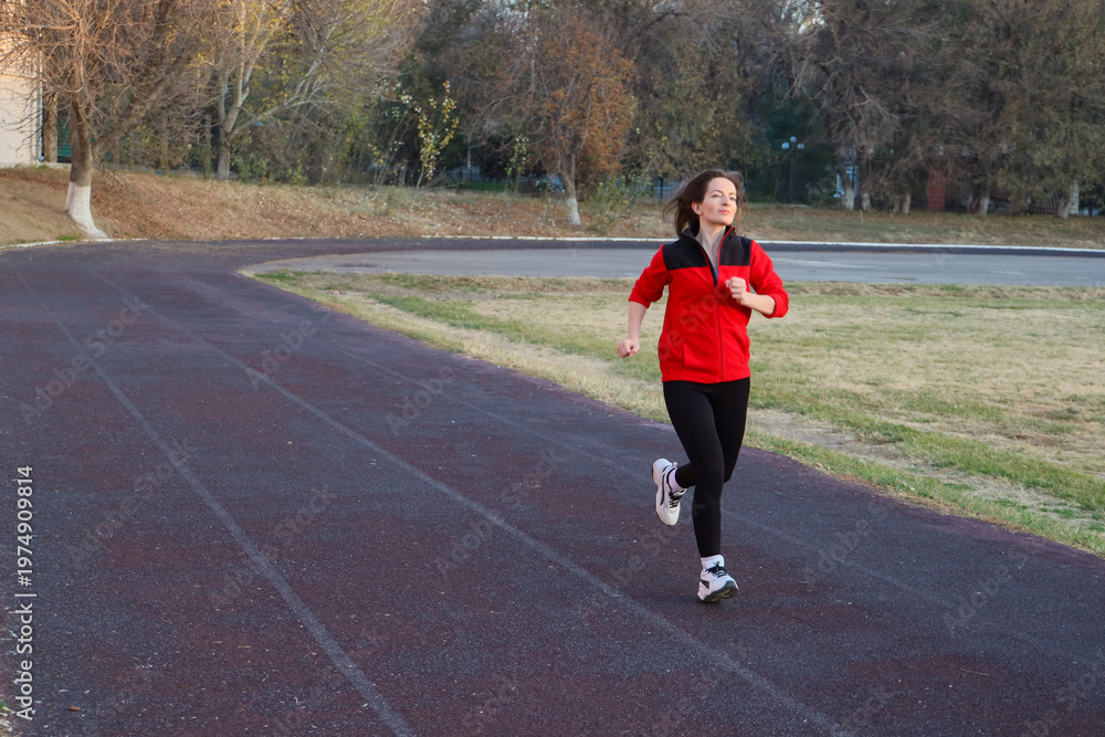 Fototapeta premium Fit mid adult woman 40s running on an outdoor track, wearing a vibrant red sports uniform