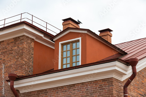 A red roof dormer with a multi-pane window and brick chimneys on a historic urban building, highlighting architectural textures, warm earth tones and classic exterior details against an overcast sky