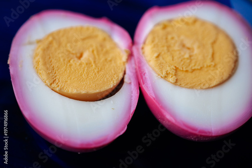 Macro close-up of two halved pickled eggs with vivid pink outer whites and firm golden yolks on a dark plate. High detail texture with minimal background.