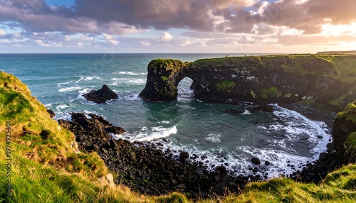 Scenic coastal view of a natural stone arch, with lush green cliffs and breaking waves under a cloudy sky