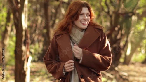 Red-haired woman in autumn park wearing coat, jeans and scarf