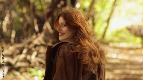 Red-haired woman in autumn park wearing coat, jeans and scarf