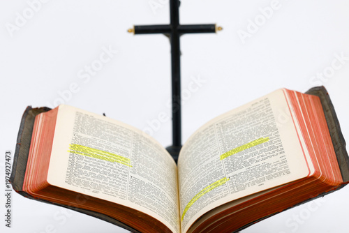  Aged scripture book on a lectern with highlighted passages and a silver crucifix behind.