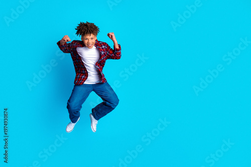 Photos Happy teenage boy jumping with joy on bright blue background wearing casual plai