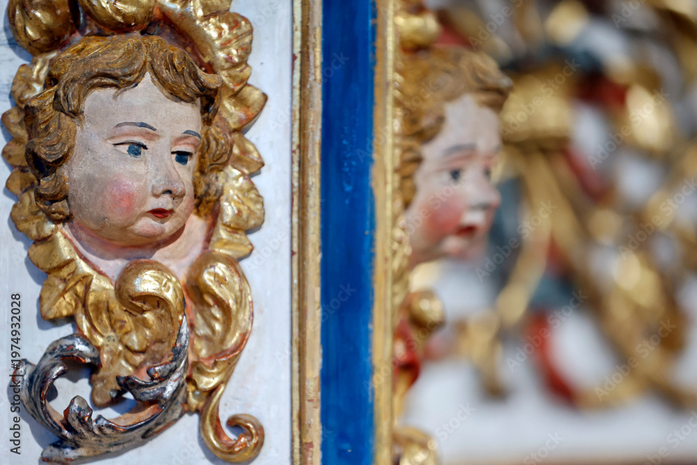 Fototapeta premium Baroque chapel of La Gruvaz after restoration. Two contrasting cherub head sculptures in polychrome wood face each other on retable. Saint Gervais. France.