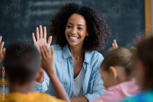 Female african adult teacher smiling while raising hand with seated diverse children in classroom engaged during lesson