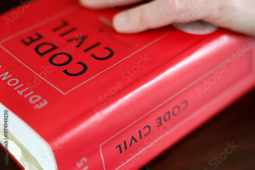 A hand rests solemnly on the red cover of a French Code Civil legal reference book.