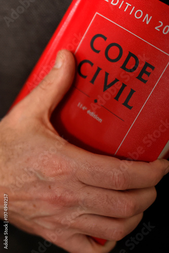 A hand rests solemnly on the red cover of a French Code Civil legal reference book.