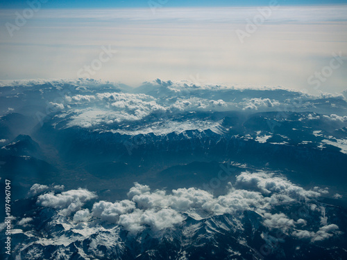 Фотография Aerial view of the Alps mountains from airplane window above clouds