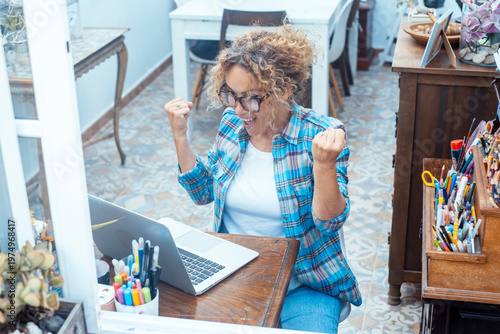 Excited woman celebrating success while working on laptop in a bright home office space