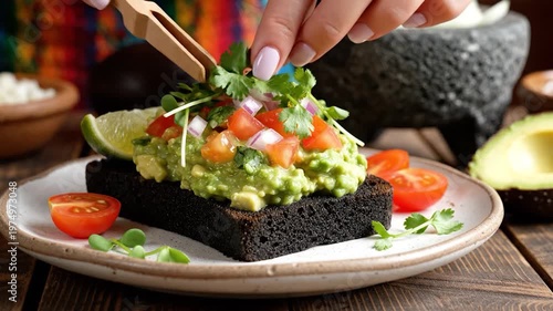 A slice of dark toasted bread topped with mashed green fruit and fresh vegetables