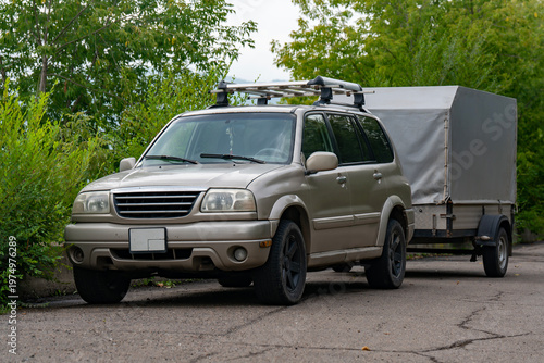 Parked SUV With Covered Trailer and Roof Rack on Rural Road Surrounded by Green Trees