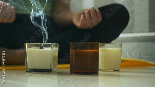 Close up of extinguished candle with smoke rising in soft light. Cozy home atmosphere, meditation, relaxation and mindfulness concept with blurred woman in background. 