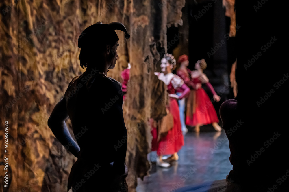 Obraz premium Male dancer in jester hat backstage watching female performers