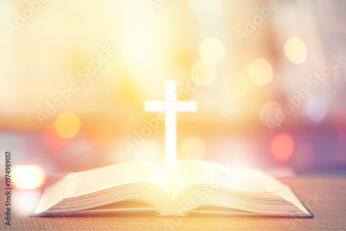 Glowing cross above open book with soft bokeh spiritual background