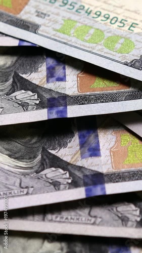 Vertical orientation of US currency hundred dollar banknotes falling on a pile of cash, representing wealth, banking, and success