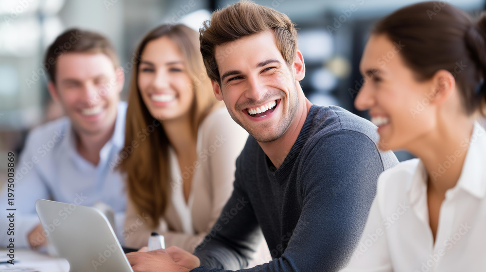 Obraz premium Group of young professionals laughing together during a meeting at a table with a laptop and documents, team bonding and collaboration concept, defocused background, with copy space