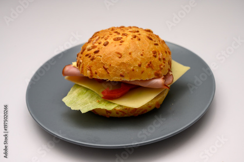 A sandwich is prepared with ham, cheese, lettuce, and tomato placed between a sesame seed bun. It is served on a blue plate