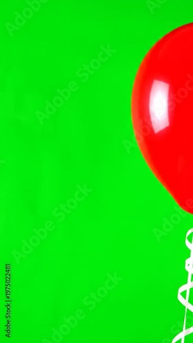 A single bright red balloon with a white ribbon isolated against a vibrant green background