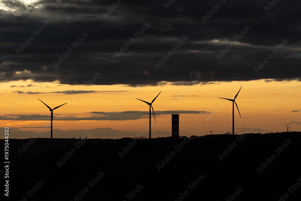Obraz premium Wind energy turbines creating silhouette against colorful sunset sky