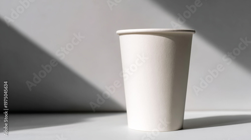 White paper coffee cup standing on a surface with diagonal shadows casting across a minimal background