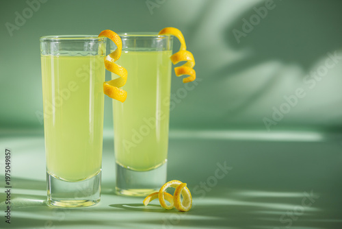 Limoncello Glasses with Curled Lemon Peels on Light Green Background.
