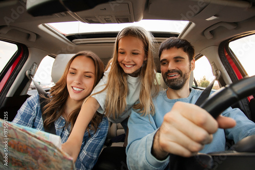 Tableau sur toile Family of three in car browsing map, father driving, mother and daughter plannin
