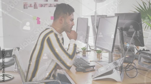 Asian worker sitting at desk, typing, thinking with network icons emerging over screens for review
