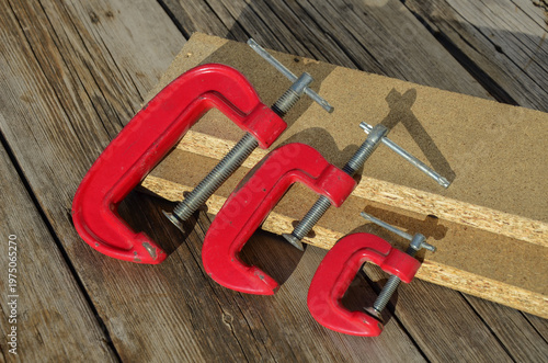 Collection of different sized G-clamps on textured wood background. Craftsmanship and DIY concept.
