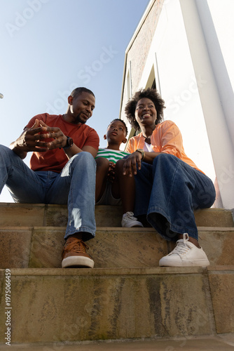 African American family with child sitting on stone steps beside white building, wearing sneakers