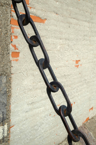 Black heavy metal chain  with elongated oval links on weathered wall closeup