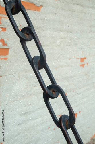 Black heavy metal chain  with elongated oval links on weathered wall closeup