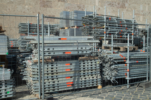Stacks of metal scaffolding parts and steel pipes at construction site behind a fence