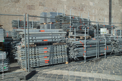 Stacks of metal scaffolding parts and steel pipes at construction site behind a fence