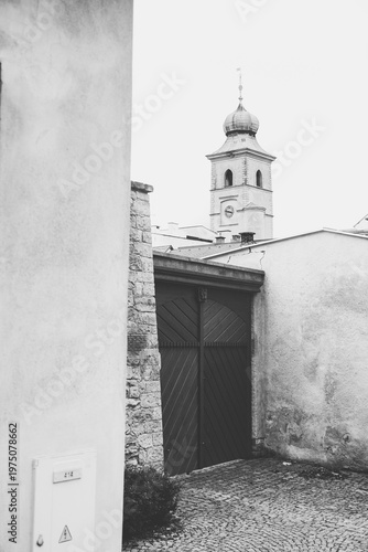 Black and white shot of a public bulletin board with event posters in Litomyšl, featuring the Old Town Hall tower and historic rooftops in the background, Czech Republic.