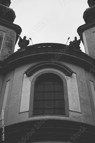 Black and white low angle view of the Baroque facade of the Piarist Church in Litomyšl, featuring arched windows and religious statues on the roof, Czech Republic.