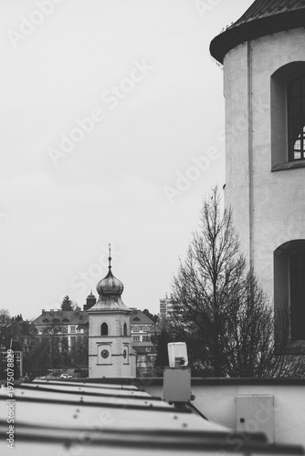 Black and white vertical shot of the Old Town Hall tower and rooftops in Litomyšl, seen from an elevated perspective with the Piarist Church wall in the foreground, Czech Republic