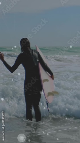 Vertical video: Surfer wading into surf with waves pushing holding pink board HUD tracking surfing