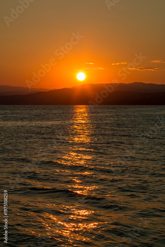 Golden sunset over a serene Aegean sea, with gentle waves and clouds illuminated by the warm evening glow.