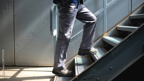 Worker climbing metal stairs in industrial facility wearing safety boots