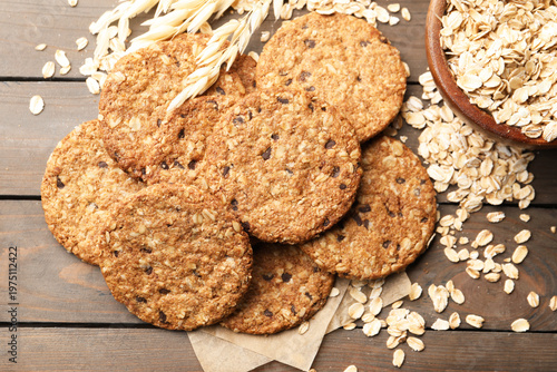 Delicious oatmeal cookies, oat flakes and spikes on wooden table, flat lay