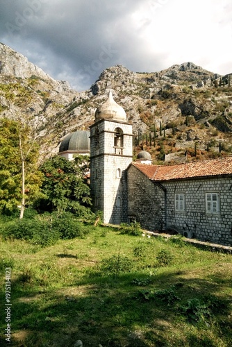 The Serbian Orthodox Church of Saint Nicholas and its bell tower in the Old Town of Kotor, Montenegro. Historic stone architecture with red tile roofs against rocky mountains and a cloudy summer sky