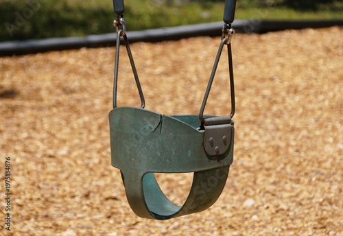 A greenish-gray bucket-style toddler swing hangs from metal chains above a wood-chip playground surface near Lake Manatee State Park, Bradenton, Florida, U.S