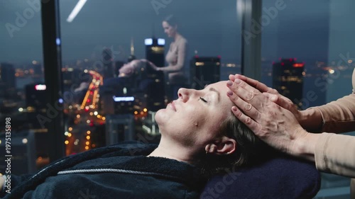 A serene woman enjoys a relaxing facial massage with a stunning cityscape at dusk in the background, exuding a sense of calm and tranquility.