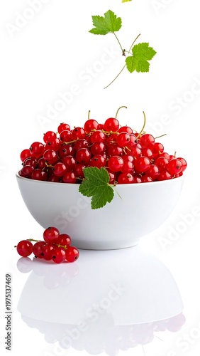 A white bowl overflows with bright red berries, some falling with leaves, set against a clean, white background