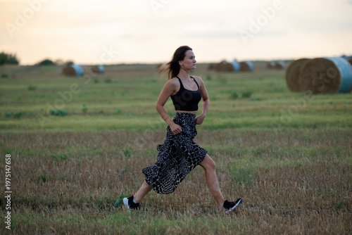 Young woman running across field at sunset, healthy lifestyle and outdoor activity