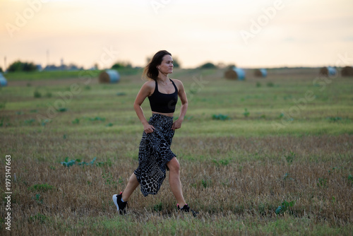 Young woman running across field at sunset, healthy lifestyle and outdoor activity