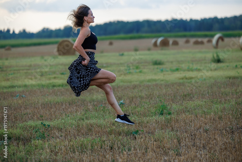 Young woman running across field at sunset, healthy lifestyle and outdoor activity